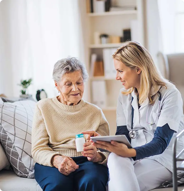 A nurse and an elderly woman sit together on a couch