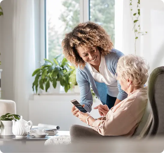 A woman assists an older woman in using her tablet,