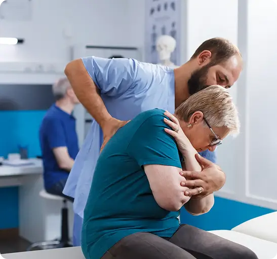 A man supports an elderly woman as she sits down